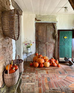 Orange pumpkins displayed on a brick porch with wooden doors and wicker baskets