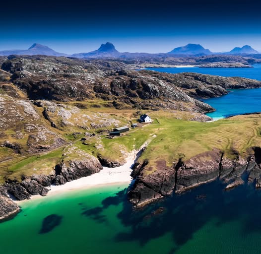 Aerial view of secluded white sand beach with turquoise water and cottage in Scottish Highlands