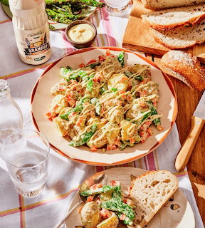 Plate of potato salad with mayonnaise and greens next to sliced bread on a checkered tablecloth