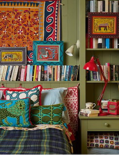 Colorful bohemian bedroom with patterned pillows, textile wall art, red lamp, and green bookshelves