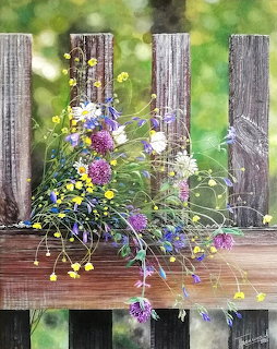 Watercolor painting of wildflowers in a basket on a wooden fence with green bokeh background