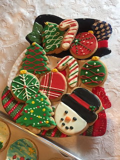 Plate of decorated Christmas cookies with trees, candy canes, ornaments, and a snowman on a white tablecloth