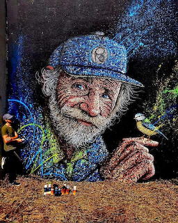 Street art mural of an old man with a beard and blue cap holding a small bird on his finger