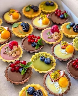 Assorted mini tarts with colorful filings and fresh fruit toppings arranged in a white box