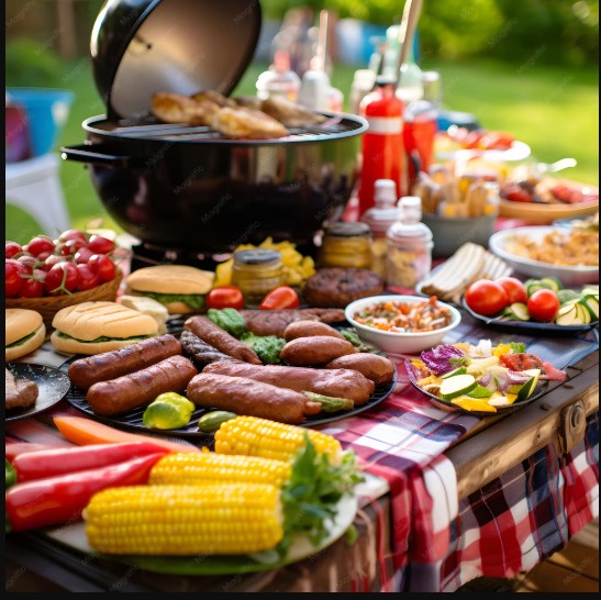 Outdoor BBQ table laden with grilled meats, corn, vegetables, and condiments on red checkered tablecloth