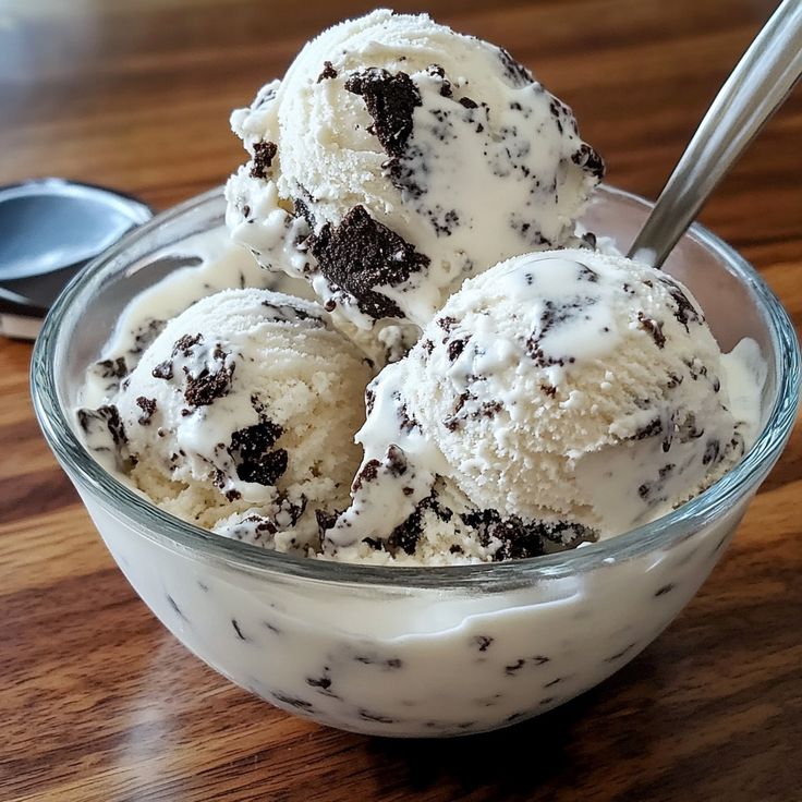 Three scoops of cookies and cream ice cream in a glass bowl with a spoon