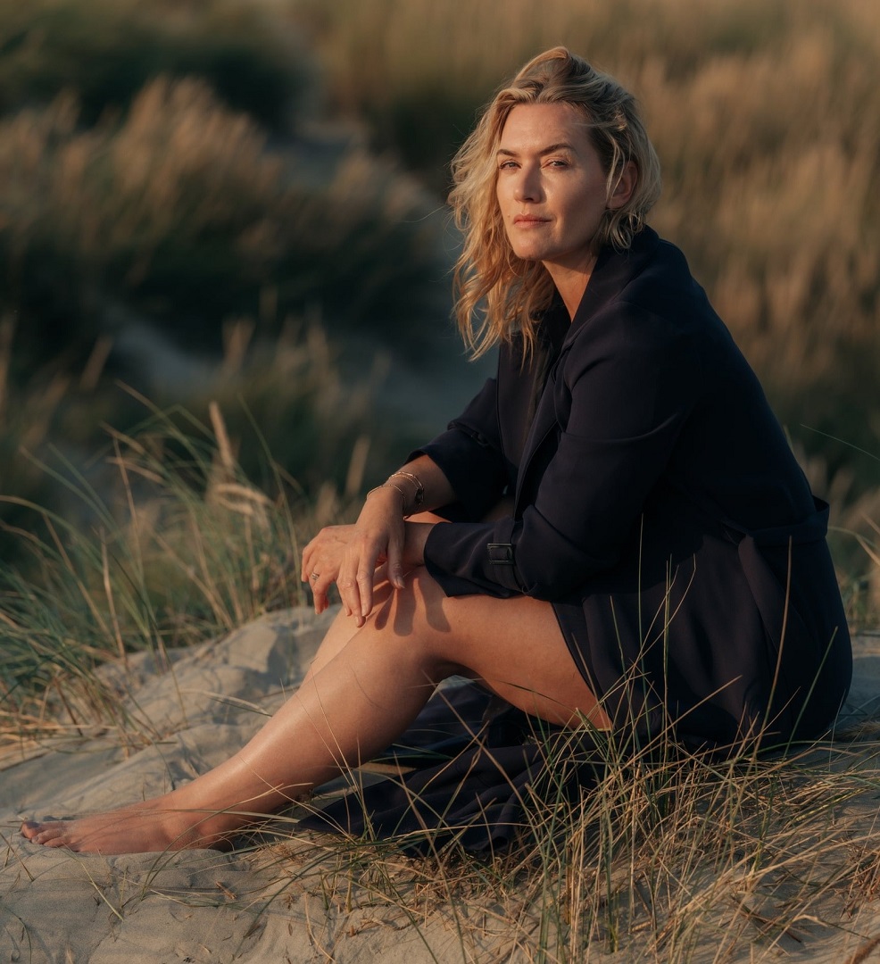Woman sitting barefoot on sandy dunes with beach grass in warm light