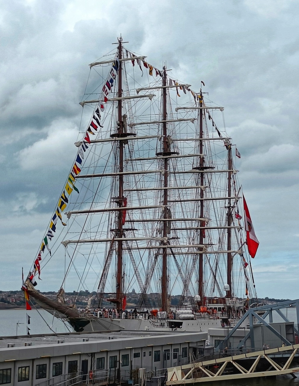 Peruvian tall ship with colorful flags on masts moored at a dock under cloudy skies