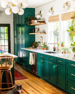 Kitchen with dark green cabinets, white counters, wooden shelves, and natural light