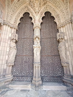 Twin carved wooden cathedral doors set in detailed stone archways with sculptures.