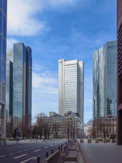 Three tall glass skyscrapers in Frankfurt's financial district along an empty urban street under blue sky