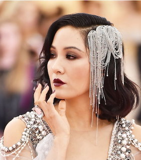 Woman with dark lipstick, smoky eyes, crystal hair piece and embellished dress at red carpet event