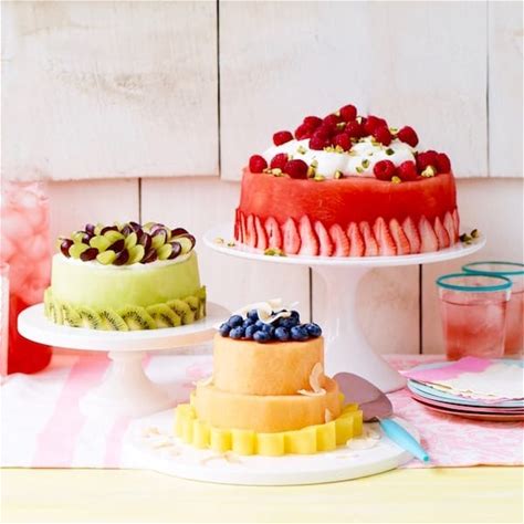 Three decorated cakes with fresh fruit toppings on white cake stands