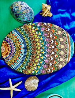 Colorful mandala dot art painted on egg-shaped stone with starfish and seashells on teal blue background