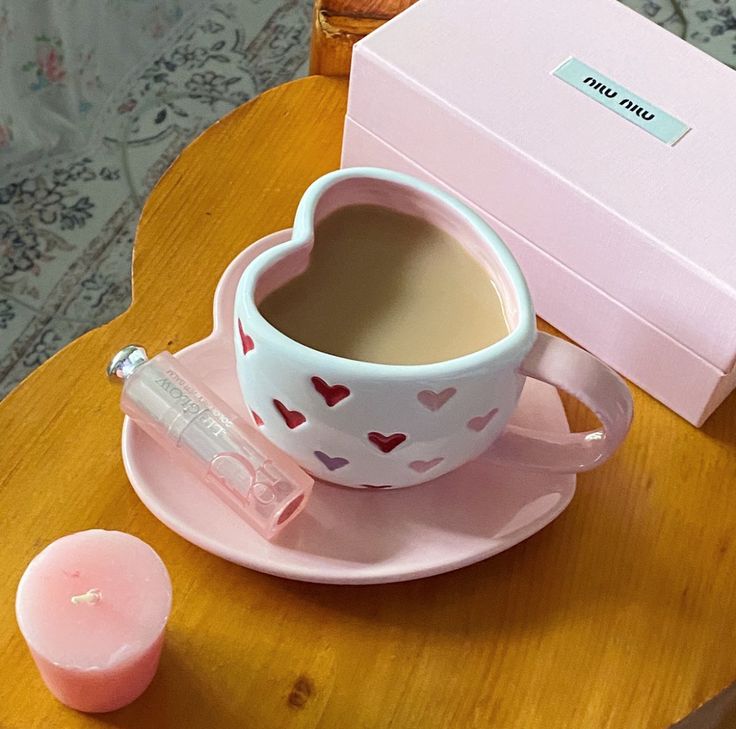 Heart-shaped white mug with red hearts filled with coffee on pink saucer with pink candle and box