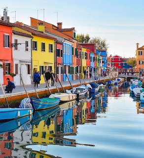 Colorful houses reflected in a canal in Burano, Italy, with moored boats along the waterfront