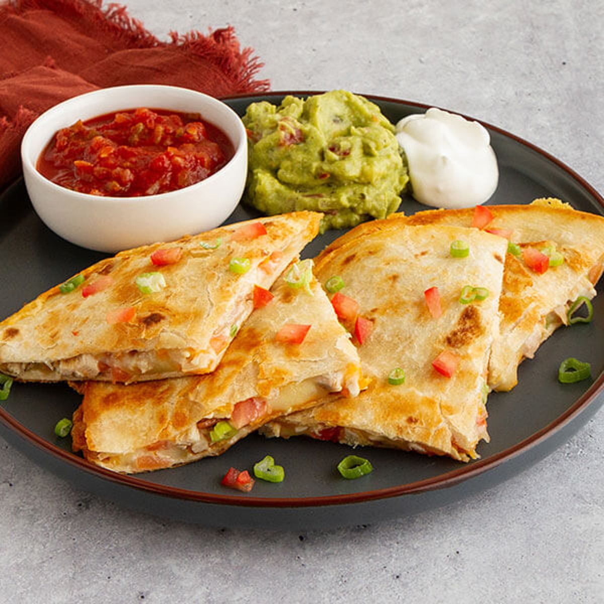 Chicken quesadilla triangles with salsa, guacamole, and sour cream on dark plate