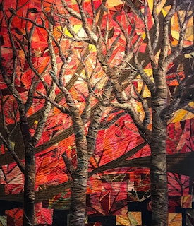 Art quilt showing autumn trees with dark branches against red, orange, and gold patchwork foliage