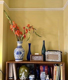 Red gladiolus flowers in blue and white vase on wooden shelf with decorative items and books