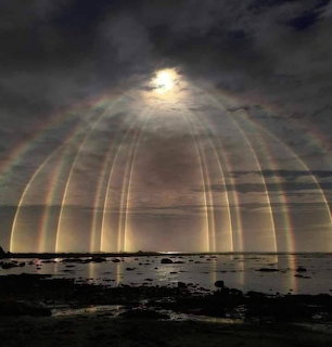 Sun shining through dark clouds over the ocean with halo-like light rays and a rocky shoreline