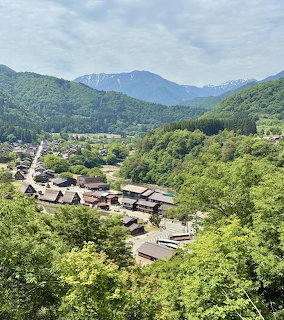 Shirakawago village in Japan with thatched houses, green hills, and distant mountains