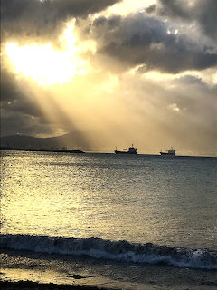 Two ships on ocean at sunset with dramatic sunbeams through stormy clouds