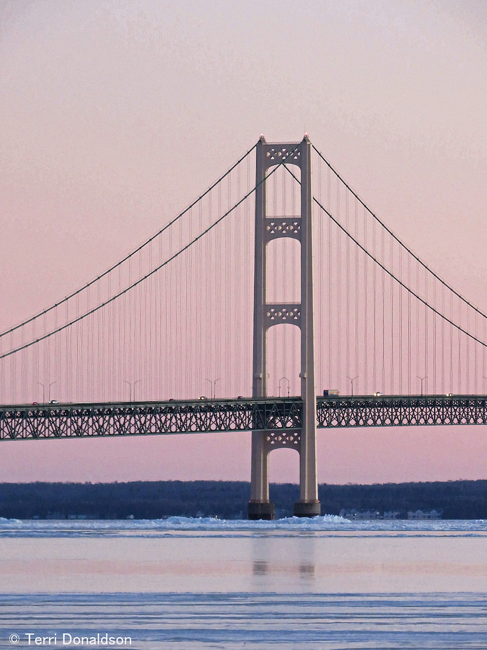 Large suspension bridge with tall towers spanning water at dusk with pink sky