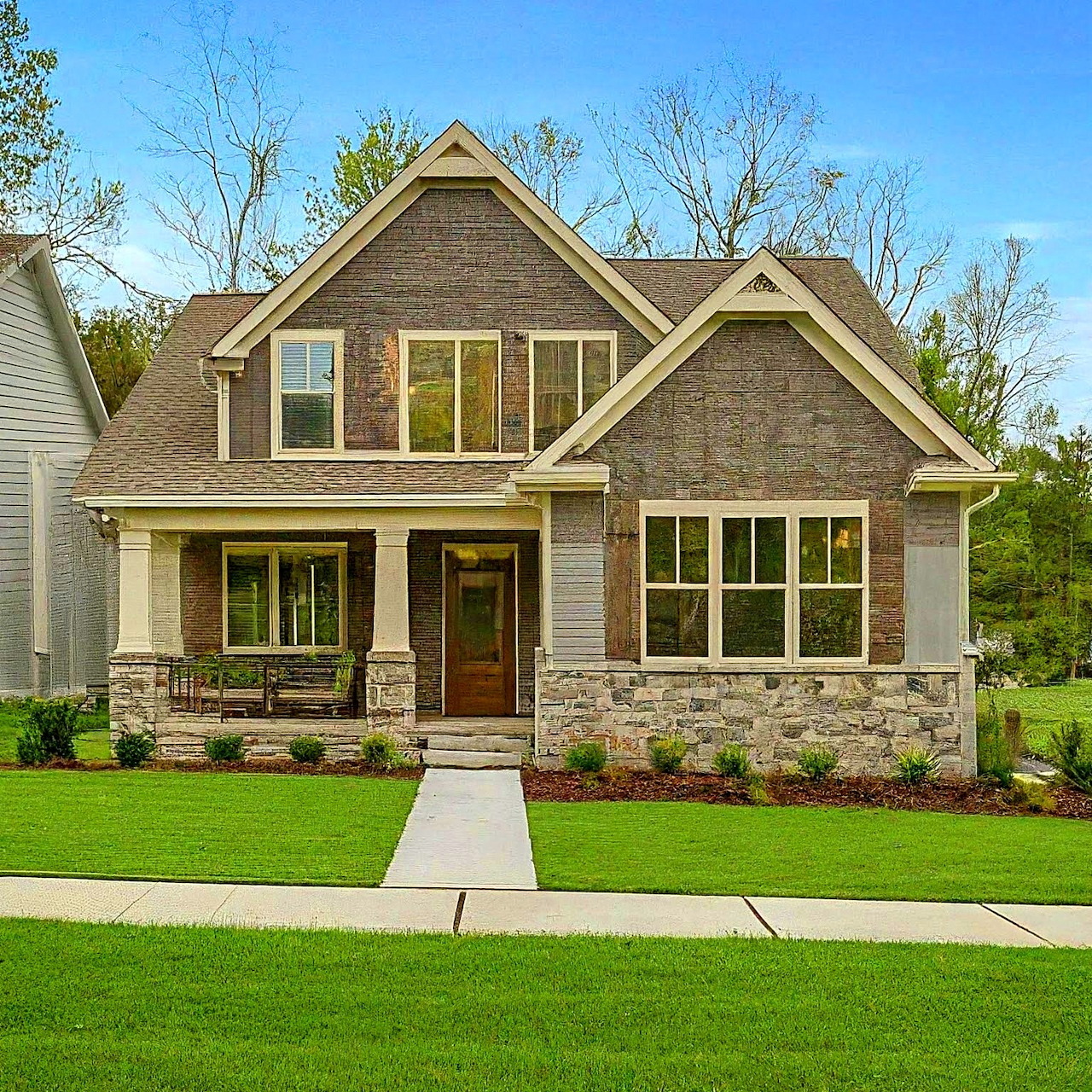 Craftsman-style two-story house with brown siding, stone base, arched gables, and green lawn