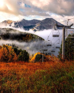 Ski chairlift on autumn hillside with fog, fall foliage, and mountains in Crested Butte, Colorado