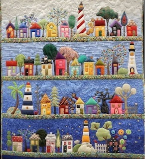 Quilted folk art depicting colorful coastal houses, lighthouses, and boats arranged in horizontal rows with patchwork sky and sea