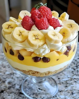 Layered trifle dessert with bananas, cream, custard, raspberries in clear glass bowl