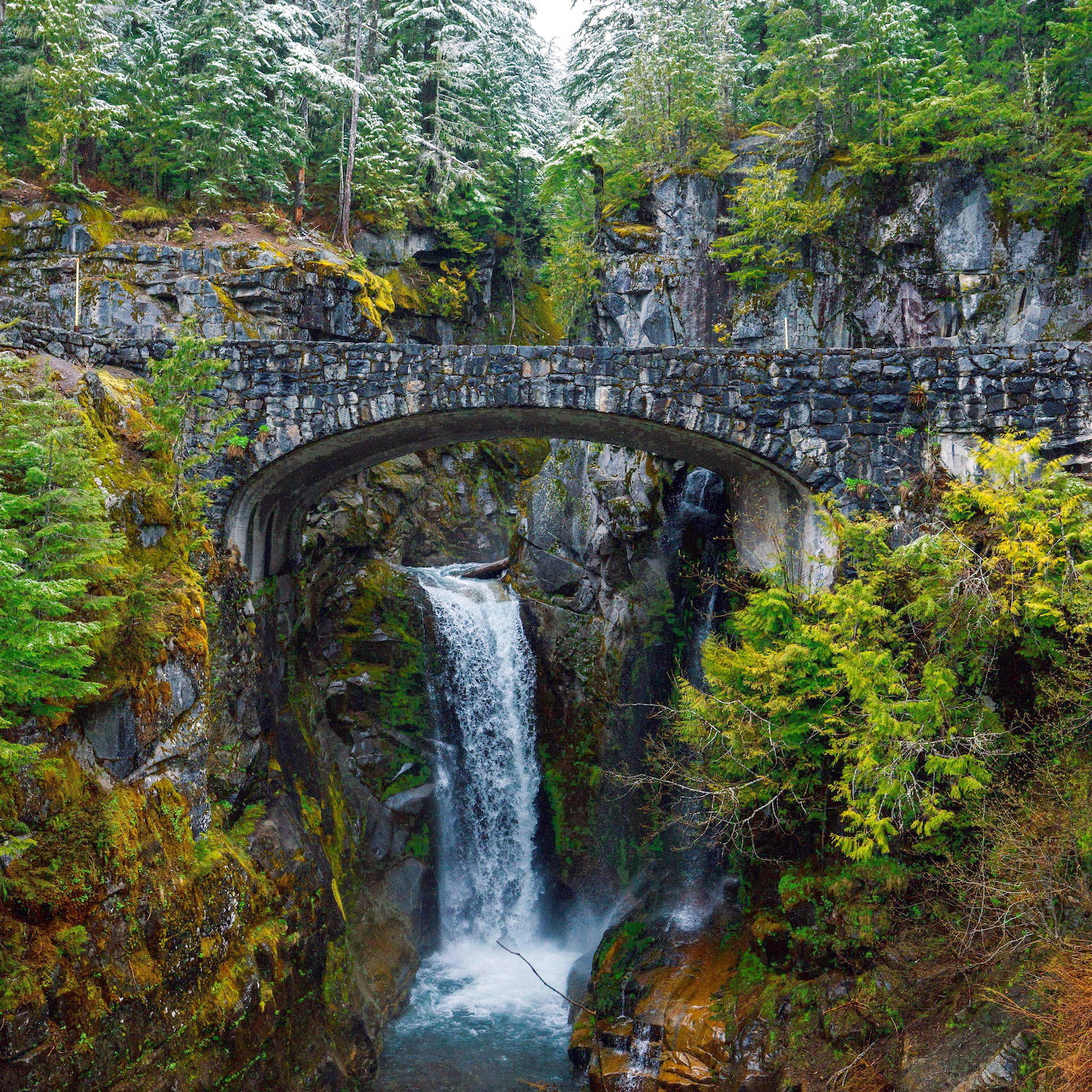 Stone arch bridge over a waterfall in a rocky forest gorge