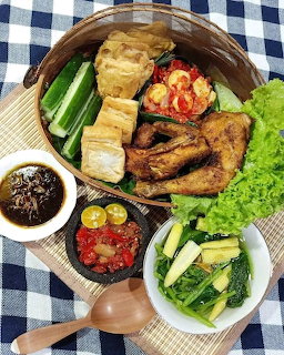 Overhead shot of Indonesian fried chicken meal with tofu, vegetables, and condiments on bamboo tray