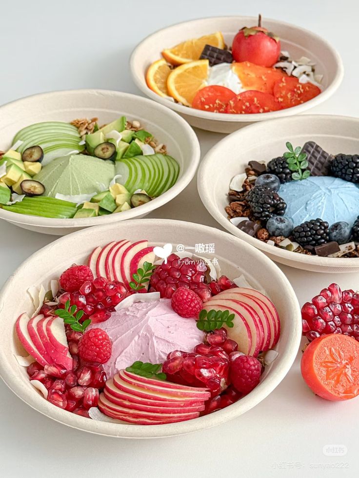 Four fruit bowls with raspberries, pomegranate, apples, oranges, and berries arranged artfully on a table
