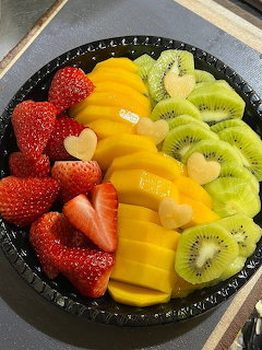 Sliced strawberries, mango, and kiwi arranged in sections on a black plate