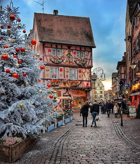 Decorated half-timbered building on a cobblestone street with Christmas tree and red ornaments at dusk