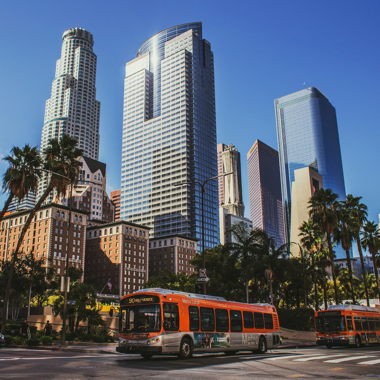 Skyscrapers, palm trees, and orange buses on a sunny downtown street