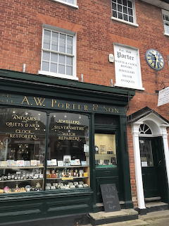 Traditional English jeweller shop with green storefront, clock, and brick building in village setting