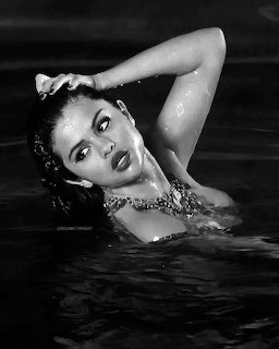 Black and white photo of a woman posing in water with one arm raised, wearing a sparkly top