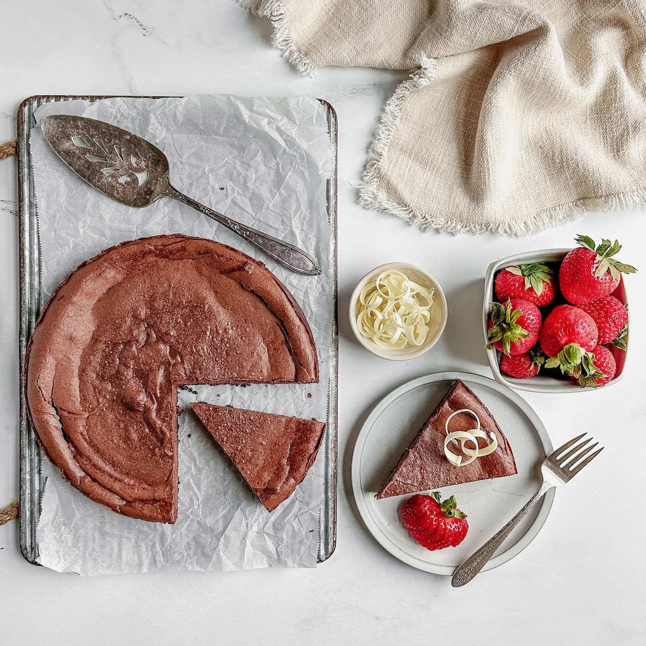 Overhead view of a chocolate cheesecake with one slice plated beside strawberries and cream