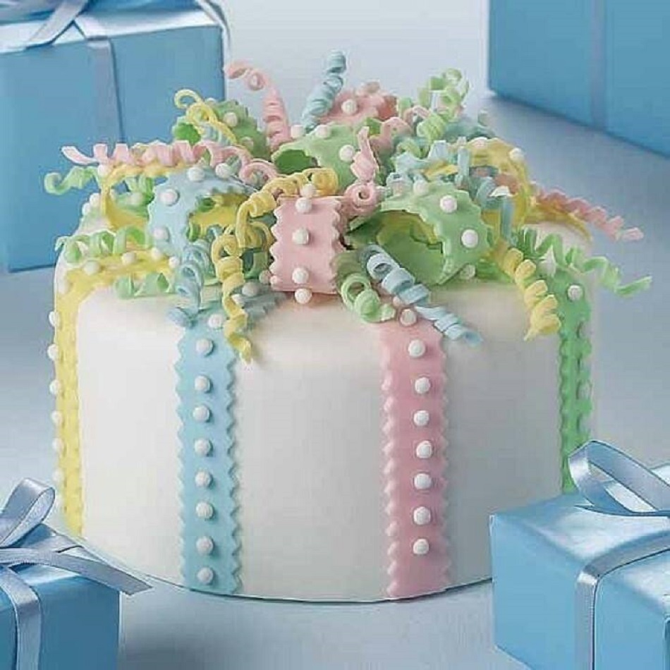 Round white cake decorated with pastel colored candy ribbons and curled toppers, blue gift boxes around it