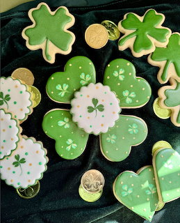 Green shamrock-shaped cookies with white icing and gold coin cookies arranged on dark green fabric