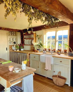 Cozy rustic kitchen with farmhouse sink, wooden table, potted plants and dried greenery on ceiling beam