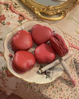Four red heart-shaped macaroons on a gold-rimmed plate with floral tablecloth and vintage mirror
