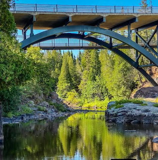 Bridge spanning a reflective river with forested banks at Gooseberry Falls State Park