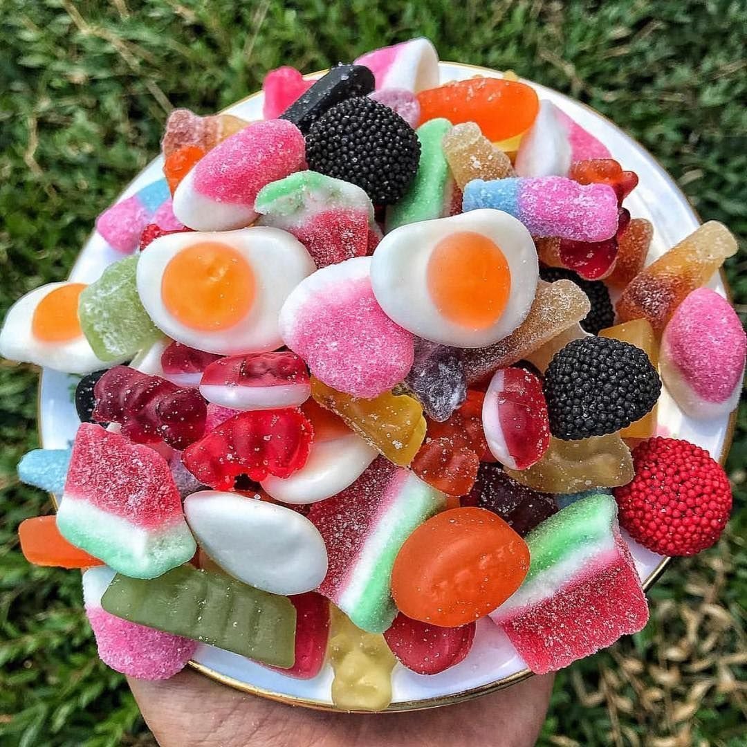 Plate overflowing with colorful gummy candies and jellies held over green grass