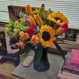 Mixed flower bouquet with sunflowers, roses, and lilies in blue vase on table