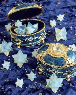 Two ornate blue jewelry boxes decorated with gold moons and stars, surrounded by white star ornaments on starry fabric