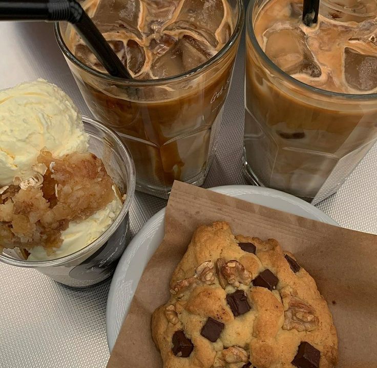 Two glasses of iced coffee with ice cream in a cup and a chocolate chip cookie in a paper box