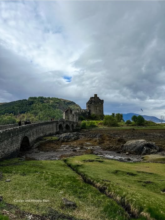 Eilean Donan Castle with stone bridge, green landscape and dramatic cloudy sky, Scottish Highlands